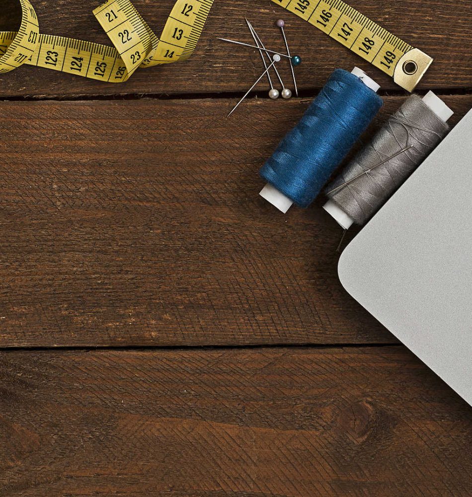 Schneiderwerkzeuge wie Schere, Nähgarn und Maßband neben einem Laptop auf einem Tisch.