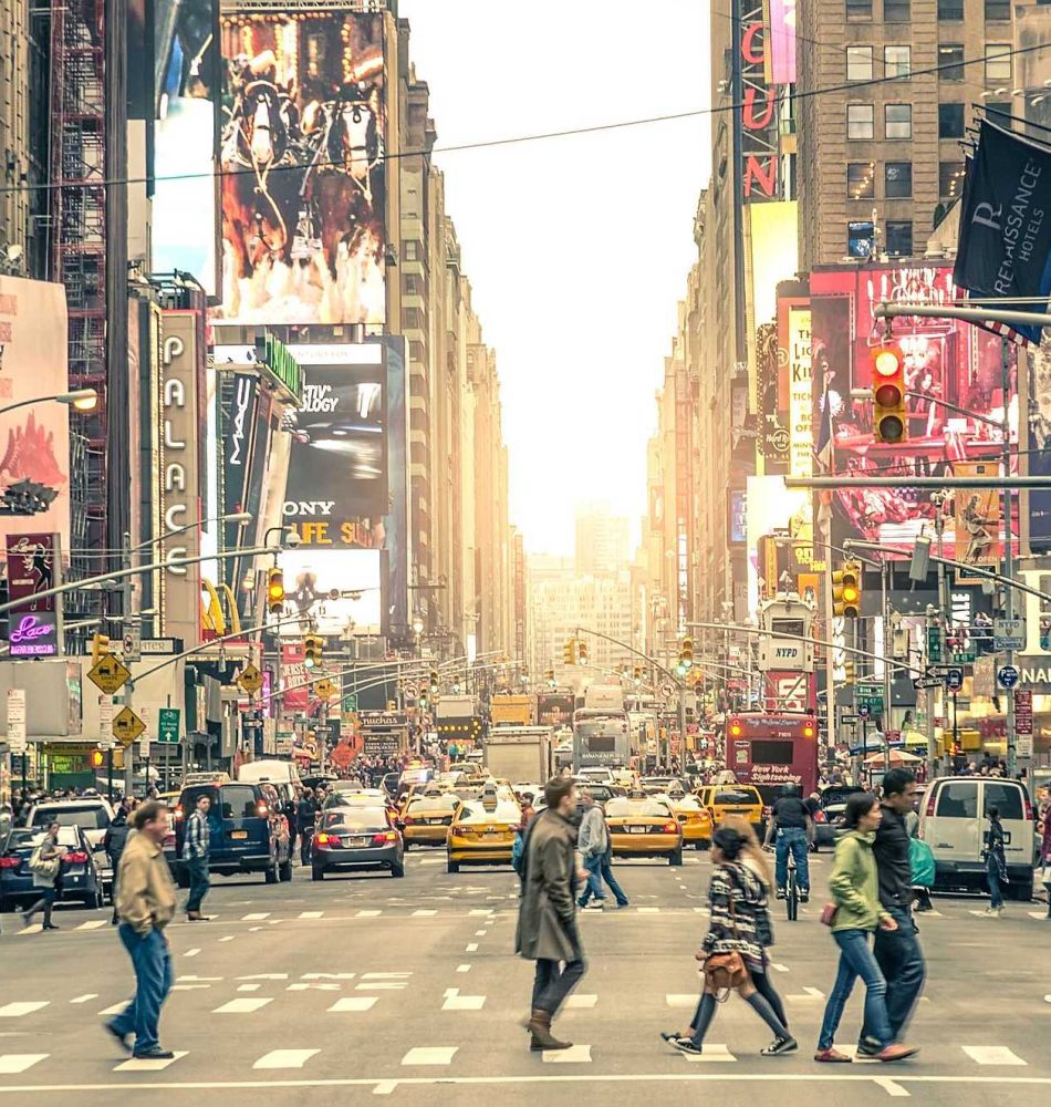 Menschen überqueren die Straße im Times Square, umgeben von großen Werbetafeln und Fahrzeugen.